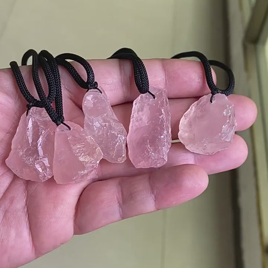Video showing hand holding natural raw rose quartz pendants, rough pink crystal necklaces with black cords for crystal wholesale