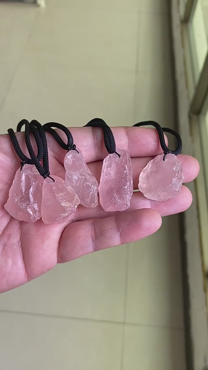 Video showing hand holding natural raw rose quartz pendants, rough pink crystal necklaces with black cords for crystal wholesale